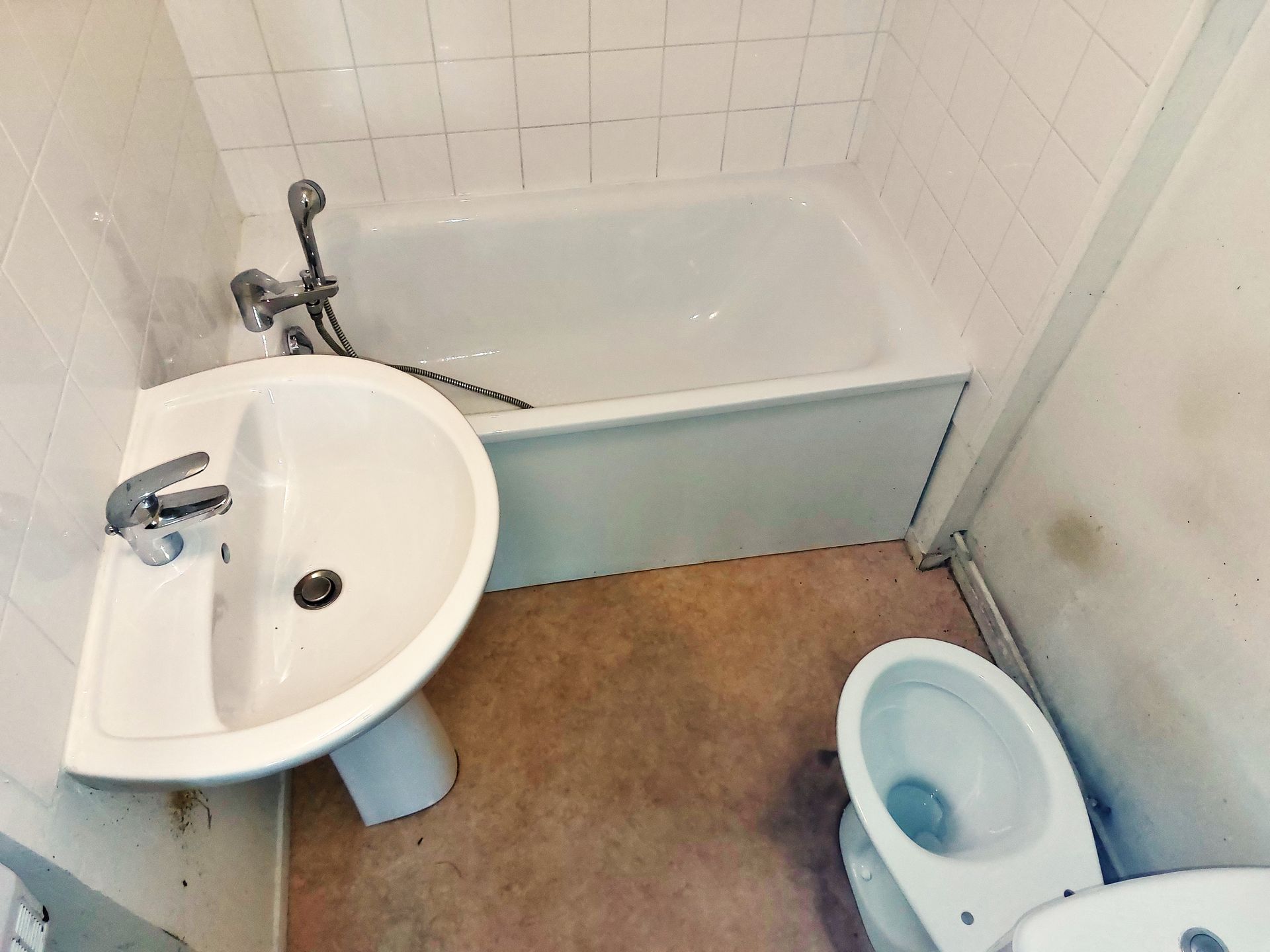 Petite salle de bains avec baignoire, lavabo et toilettes. Sol beige, robinetterie blanche et mur carrelé.
