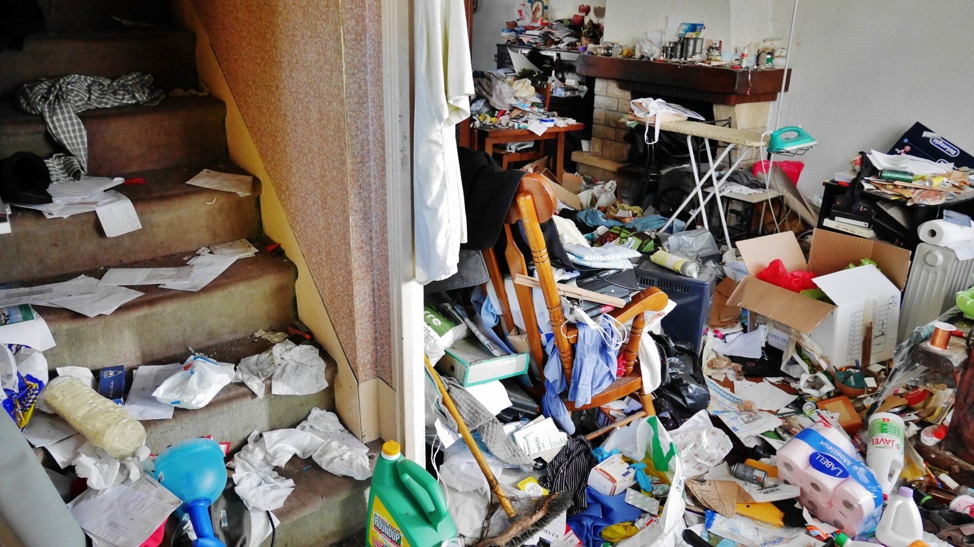 Escalier et salon encombré de déchets et d'objets.