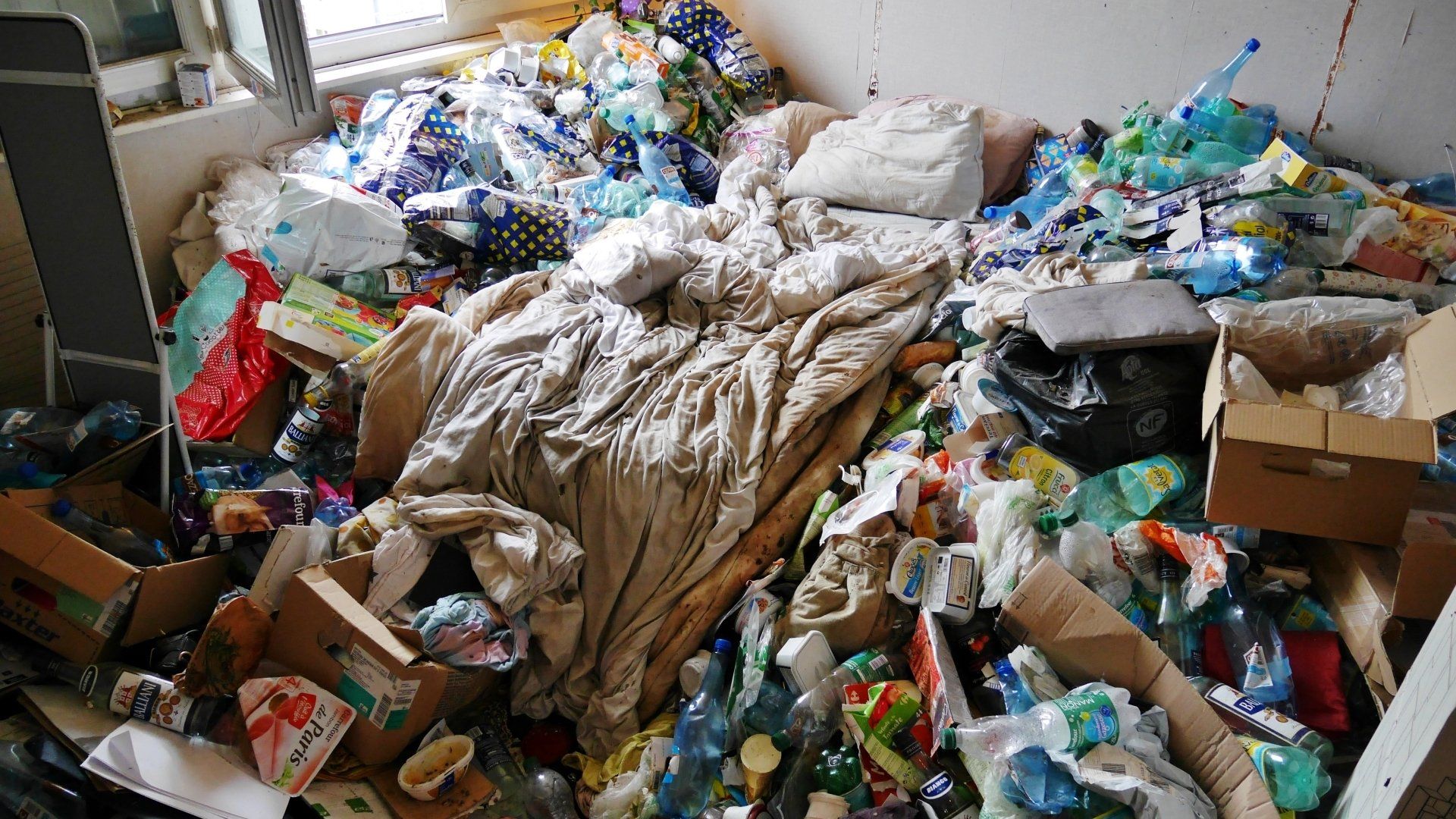 Une chambre à coucher remplie de déchets tout autour d'un lit.