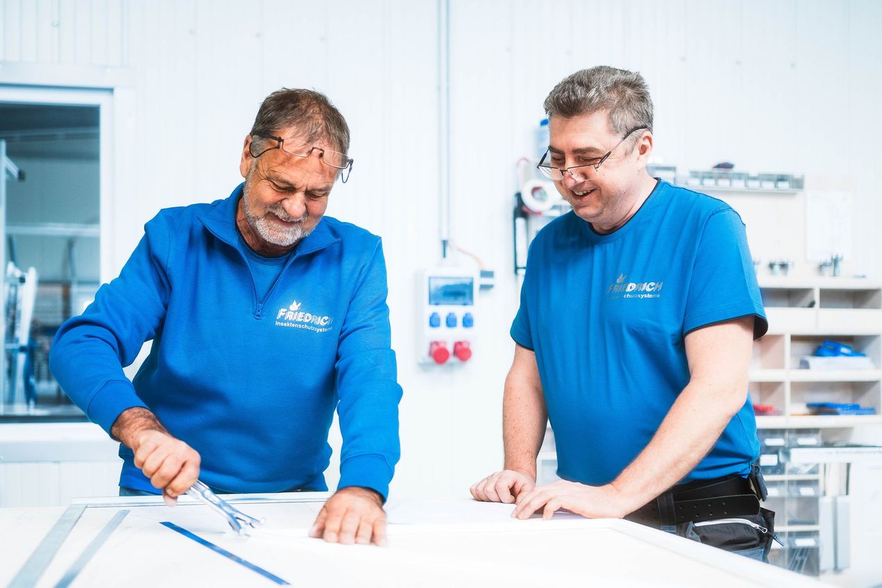 Zwei Männer in blauen Hemden stehen nebeneinander in einem Raum und schauen auf ein Blatt Papier.