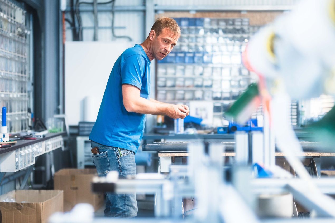 Ein Mann in einem blauen Hemd arbeitet in einer Fabrik an einer Maschine.
