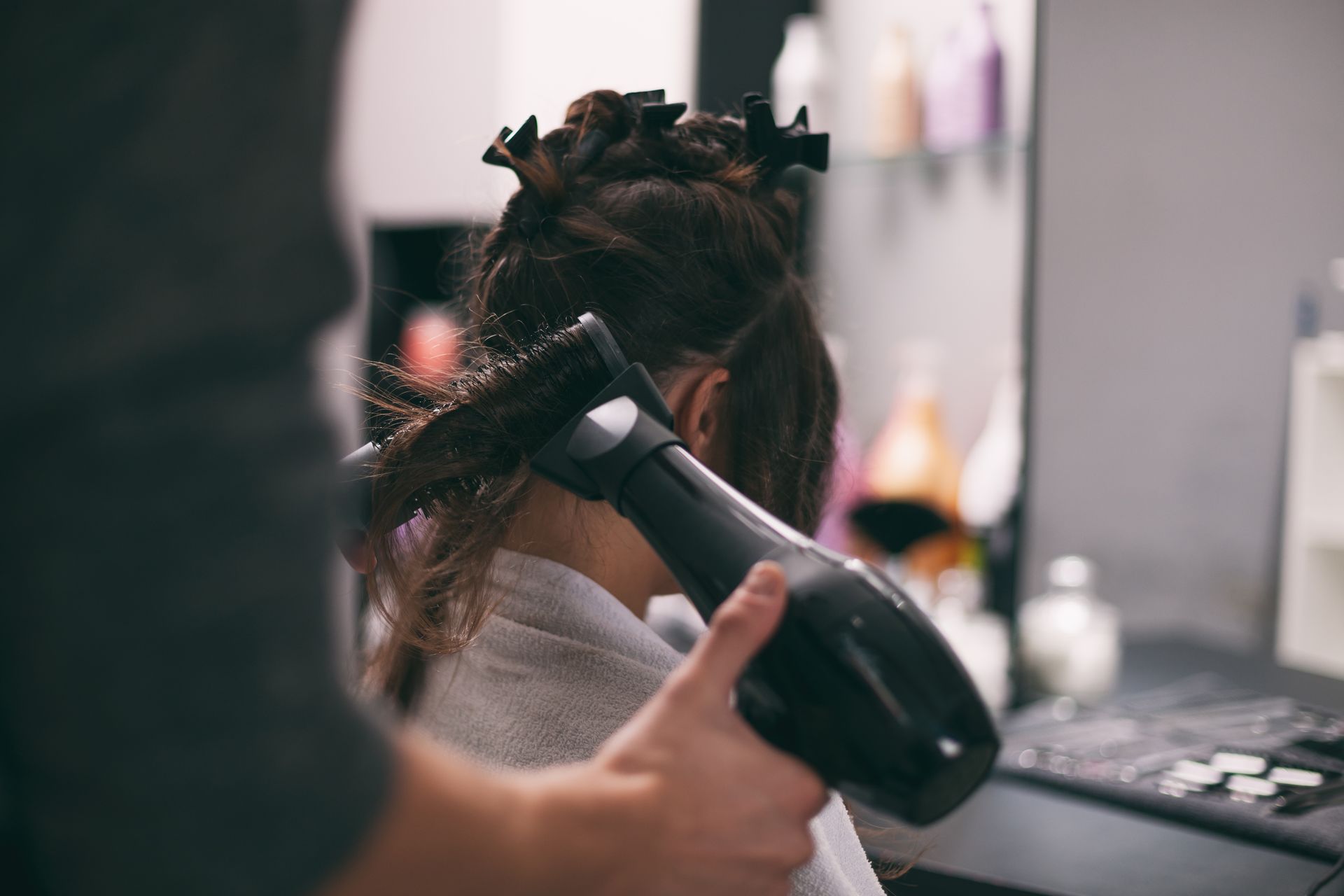 Un coiffeur sèche les cheveux d'une cliente dans un salon. La personne porte une serviette et ses cheveux sont séparés par des pinces.