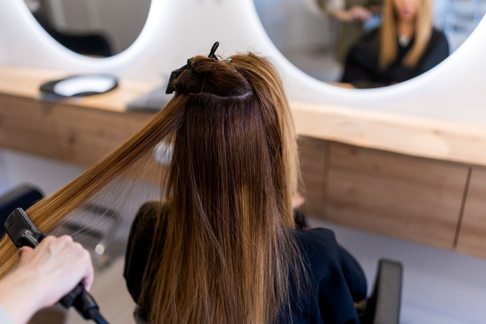 Une personne se fait coiffer dans un salon de coiffure. Un coiffeur lisse de longs cheveux bruns.