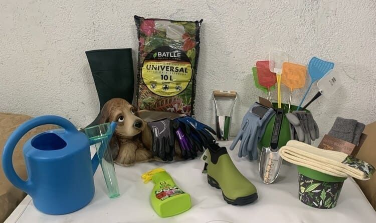 Una mesa cubierta con una regadera, botas, guantes, un trapeador y un perro.