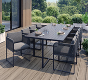 Collection Citadine. Table d'extérieur de couleur gris anthracite avec 8 fauteuils coordonnés de la même couleur sur une terrasse en bois.