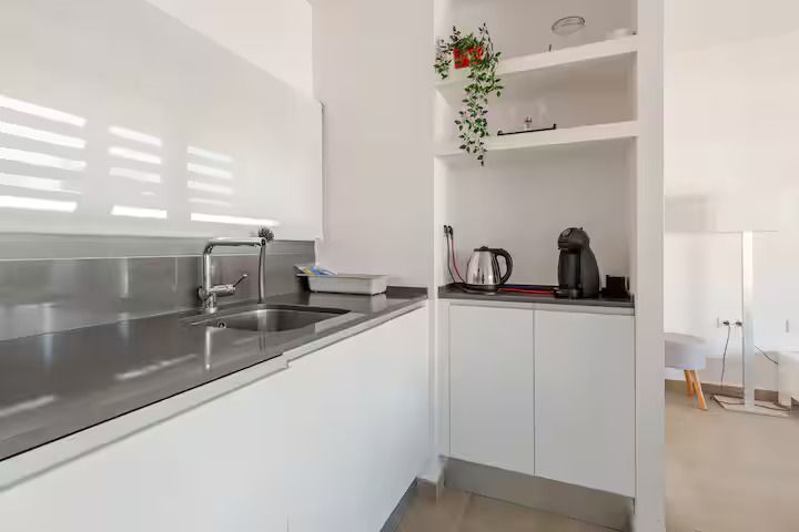 Una cocina con gabinetes blancos, un fregadero y un estante.