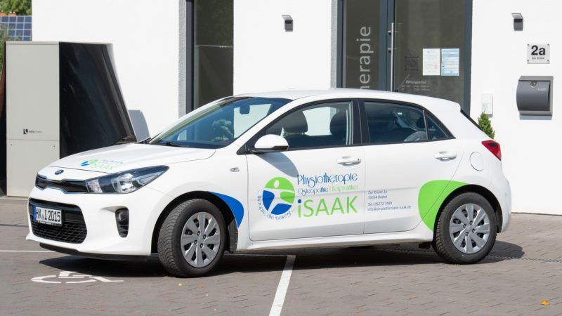 Ein weißes Auto steht auf einem Behindertenparkplatz vor einem Gebäude.