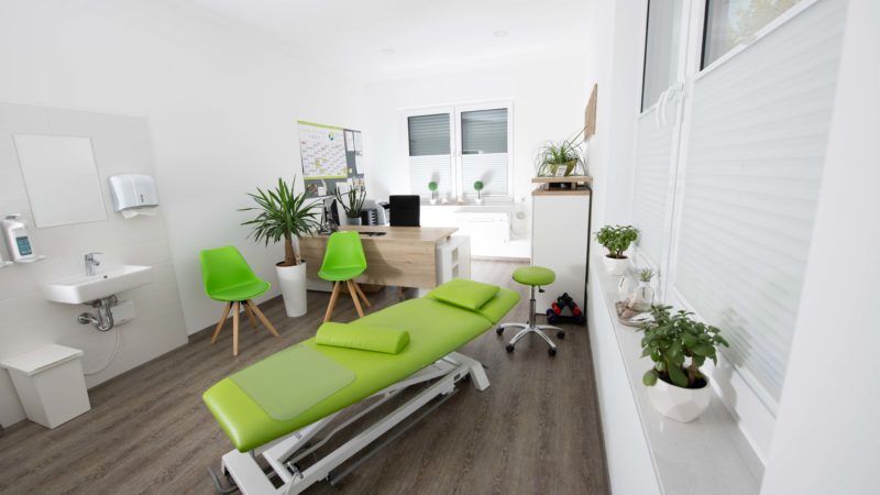 Ein Raum mit einem grünen Massagetisch und grünen Stühlen.