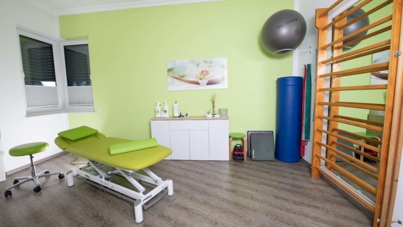 Ein Physiotherapieraum mit einem grünen Tisch und einem grauen Gymnastikball.