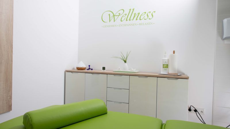 Ein grüner Massagetisch in einem Raum mit einem Schild an der Wand, auf dem „Wellness“ steht.