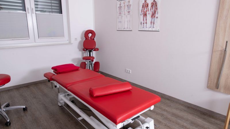 In der Mitte des Raumes steht ein roter Massagetisch.