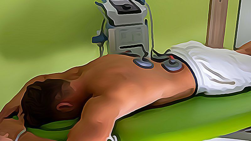 Ein Mann liegt auf einem grünen Bett und bekommt eine Massagemaschine.