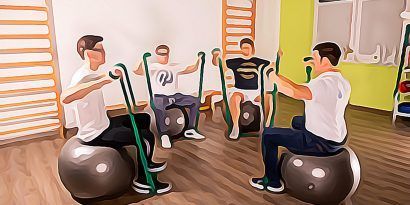 Eine Gruppe Männer sitzt in einem Fitnessstudio auf Gymnastikbällen.