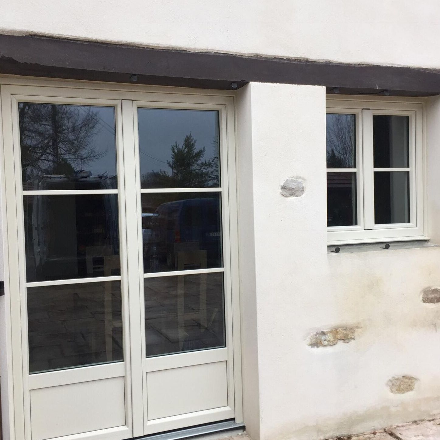 Vue extérieure d'un bâtiment avec portes-fenêtres et fenêtres aux cadres blanc cassé, sur un mur en stuc blanc.