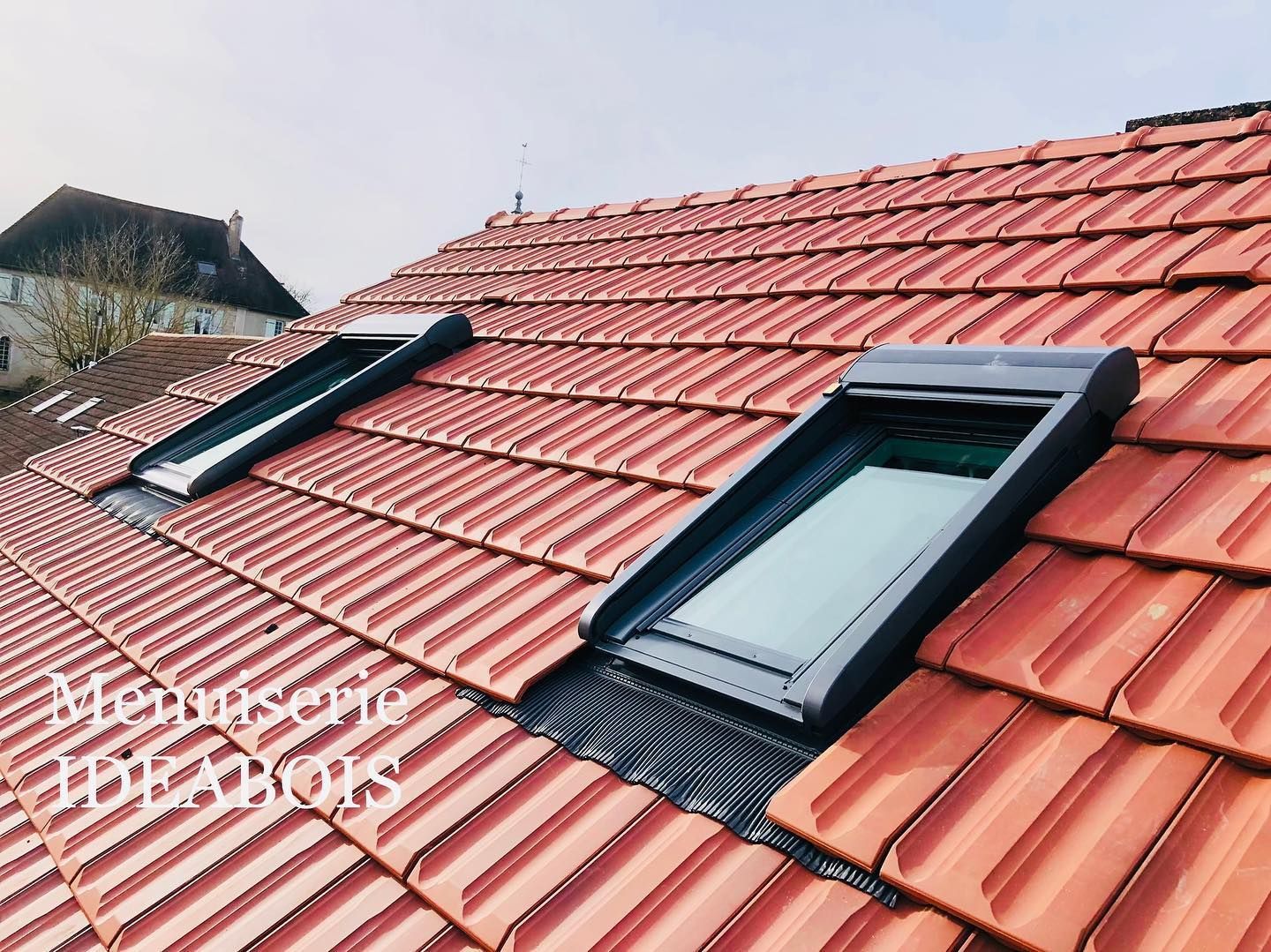 Toit en tuiles rouges avec deux puits de lumière rectangulaires.
