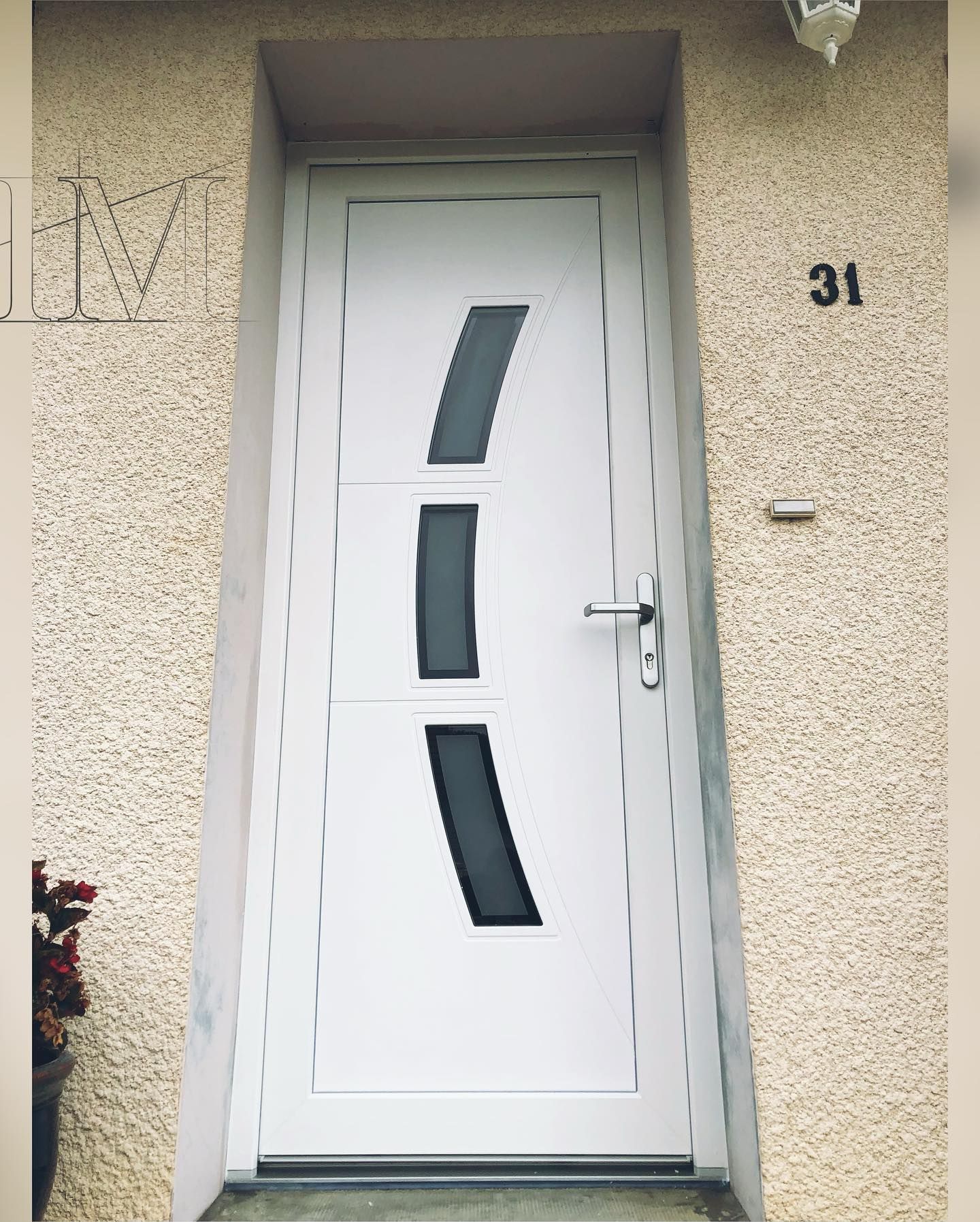 Porte d'entrée blanche avec panneaux de verre foncé, encastrée dans un mur beige, à côté du numéro 31.