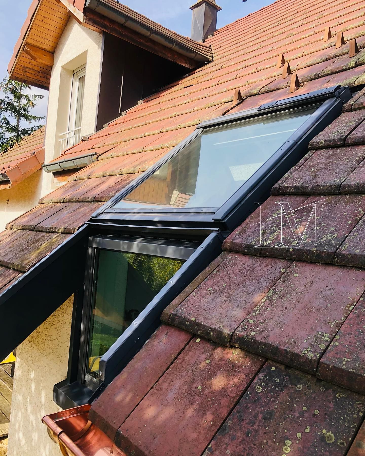 Toiture avec puits de lumière et tuiles brun orangé. Une lucarne et une gouttière sont visibles.