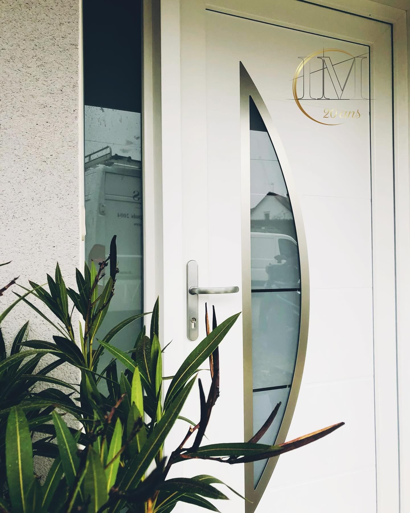 Porte blanche avec fenêtre cintrée et encadrement métallique, à côté d'une fenêtre et d'une plante verte.