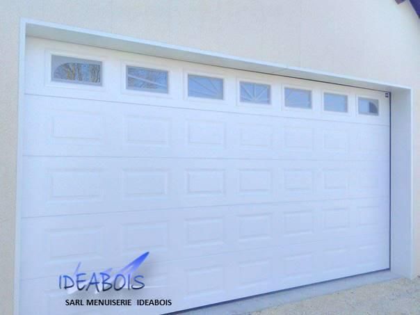 Porte de garage blanche avec fenêtres rectangulaires en partie supérieure.