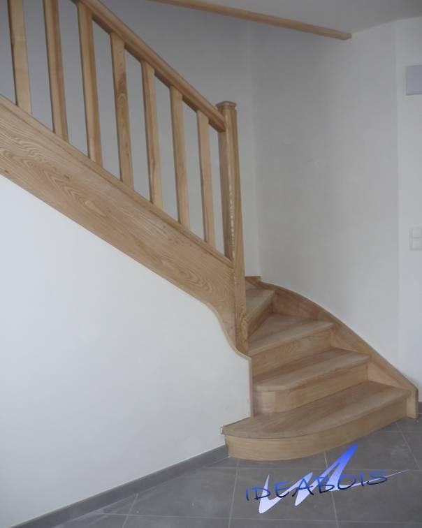 Escalier en bois contre un mur blanc, avec marches et rampe incurvées.