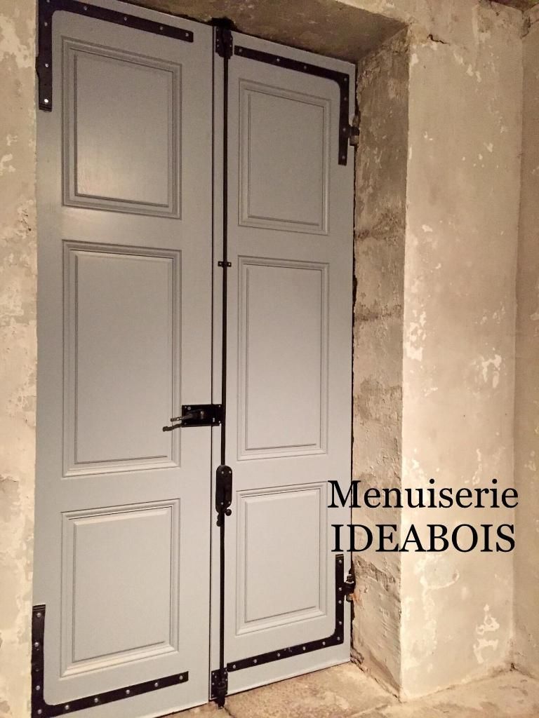 Double porte grise avec quincaillerie noire dans un encadrement de porte en pierre.