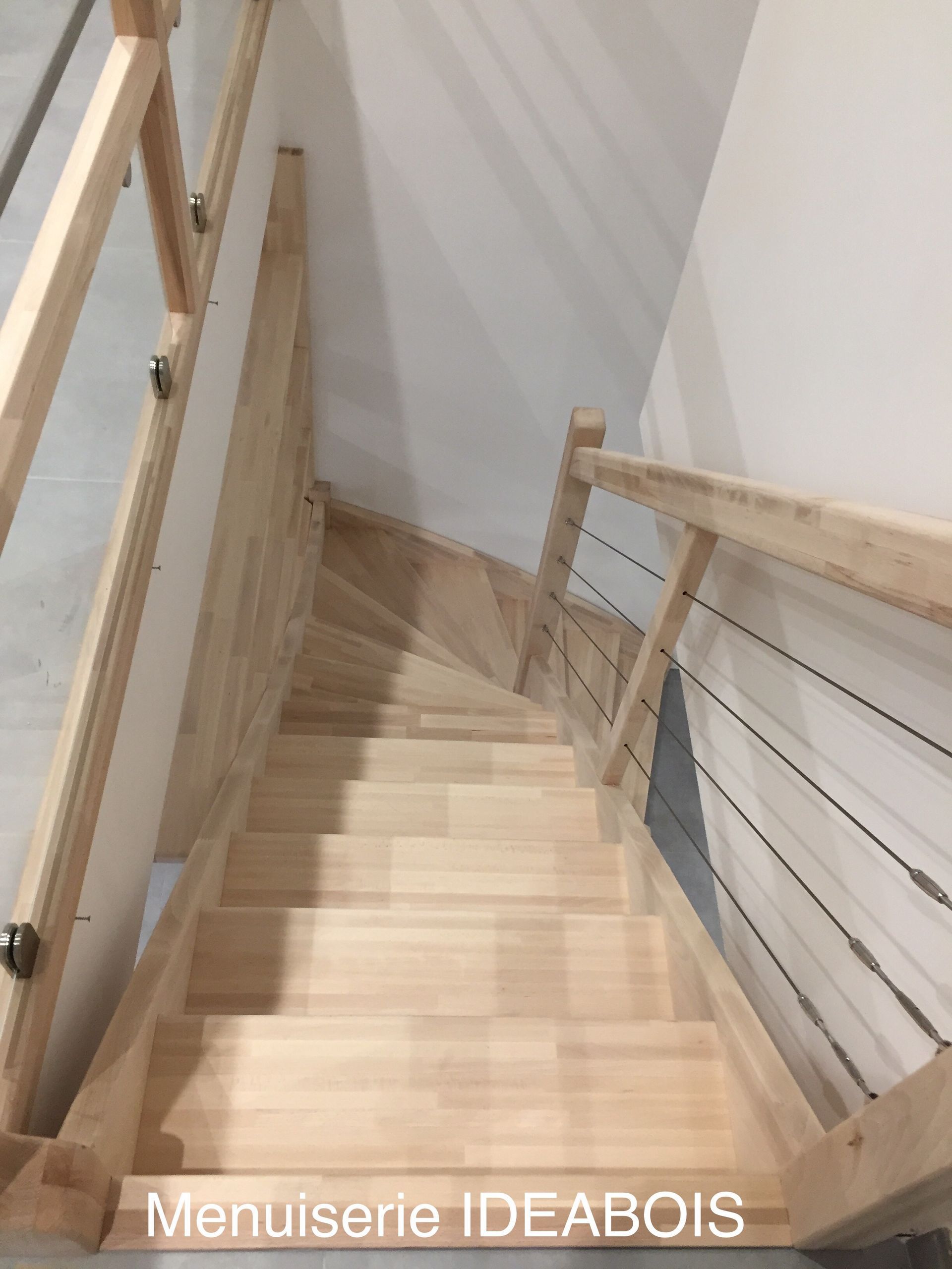 Escalier en bois avec rampe en câbles, vu du point de vue du spectateur.