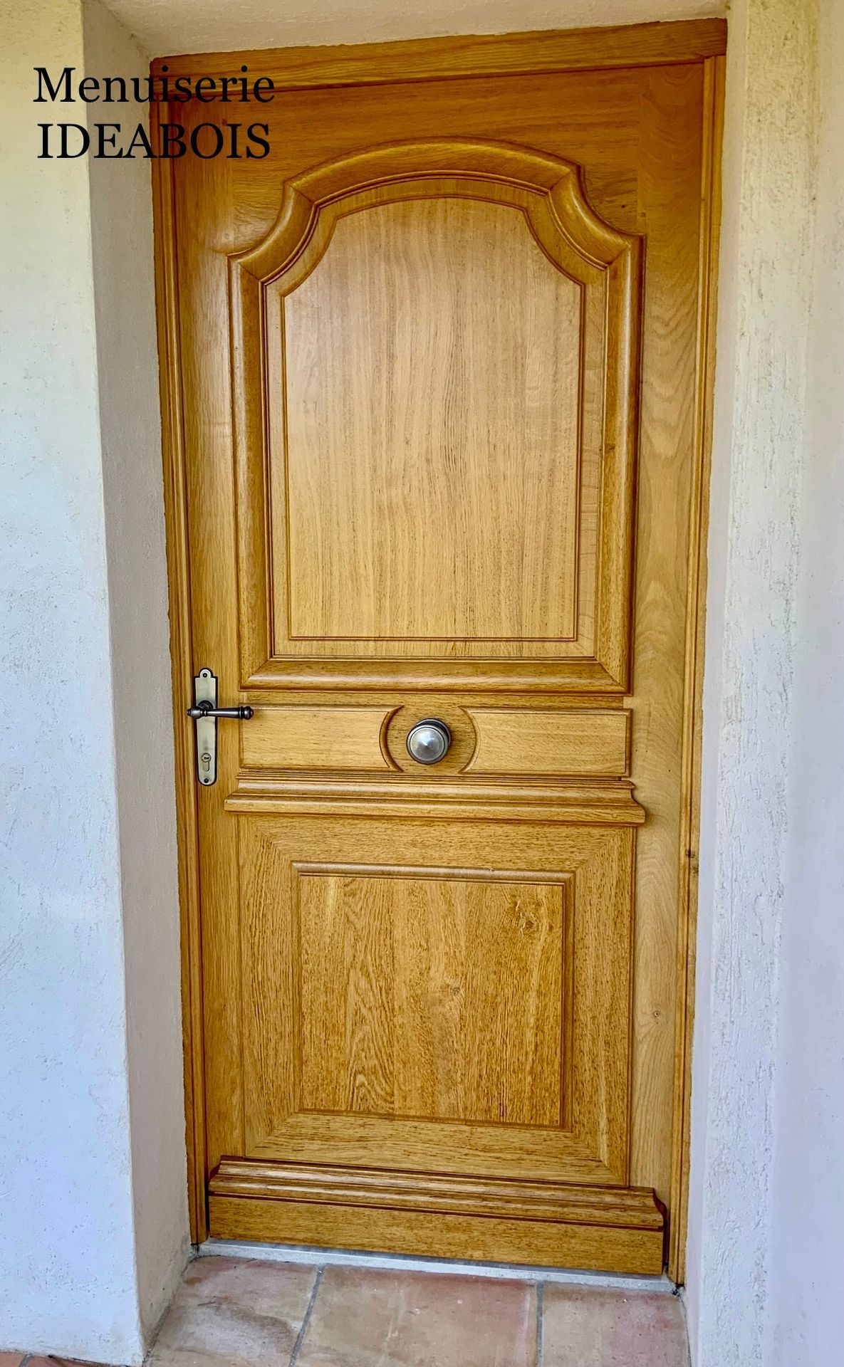 Porte d'entrée en bois avec panneaux décoratifs et poignée argentée.