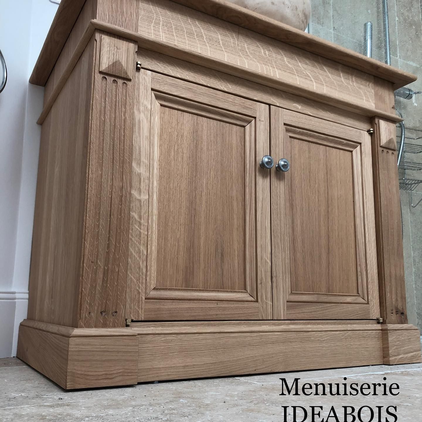 Meuble-lavabo en bois avec deux portes, poignées en cristal et moulures décoratives.