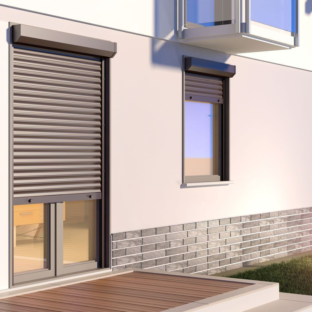 Extérieur d'un bâtiment avec des volets roulants sur deux fenêtres, intégrés dans un parement en pierre.