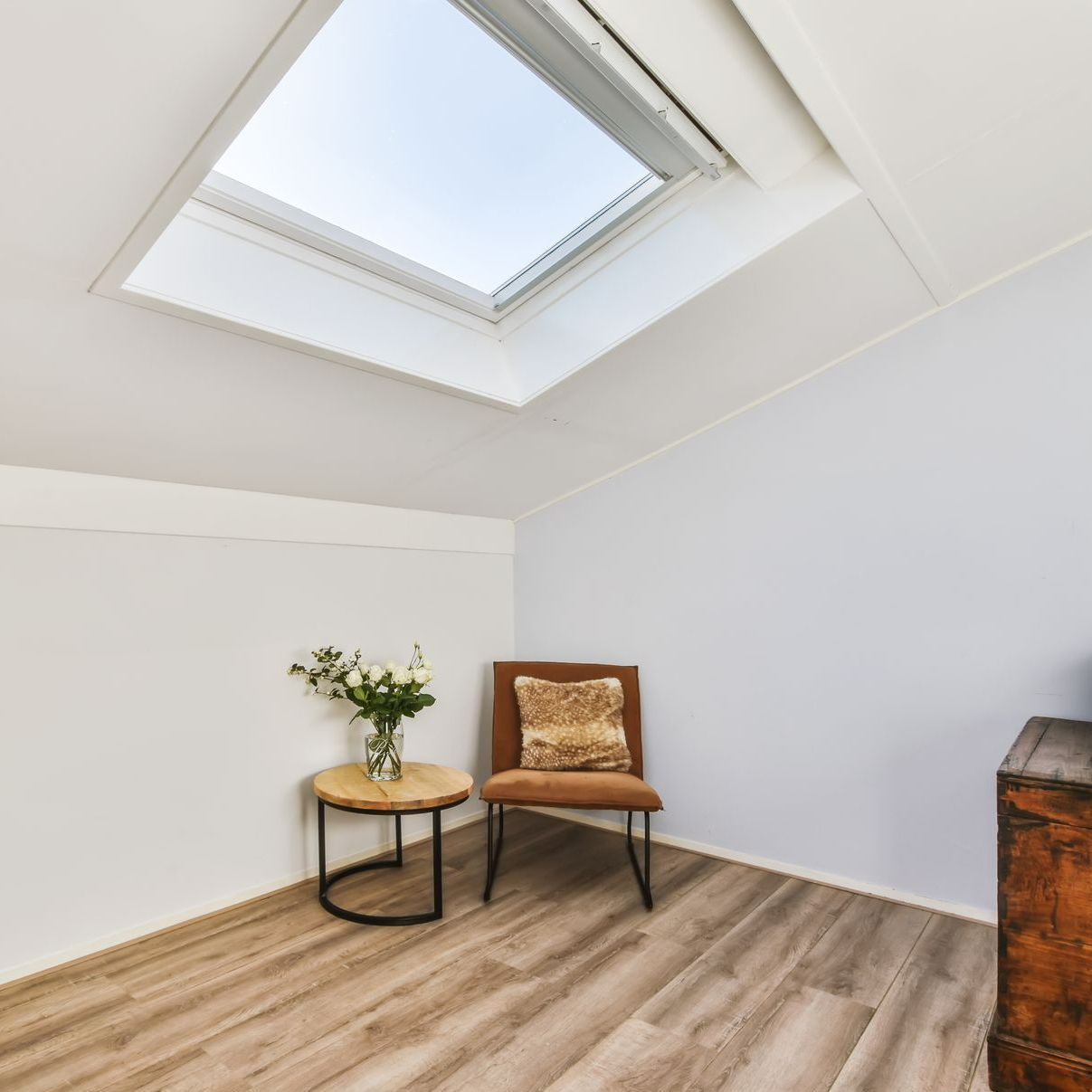 Une pièce avec puits de lumière, chaise, petite table avec des fleurs et parquet.