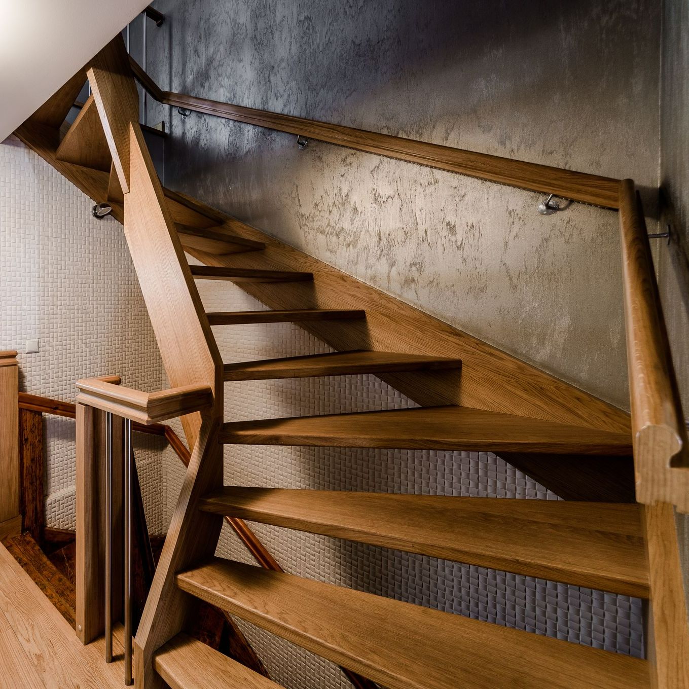 Escalier en bois avec contremarches ouvertes et rampe contre un mur gris texturé.