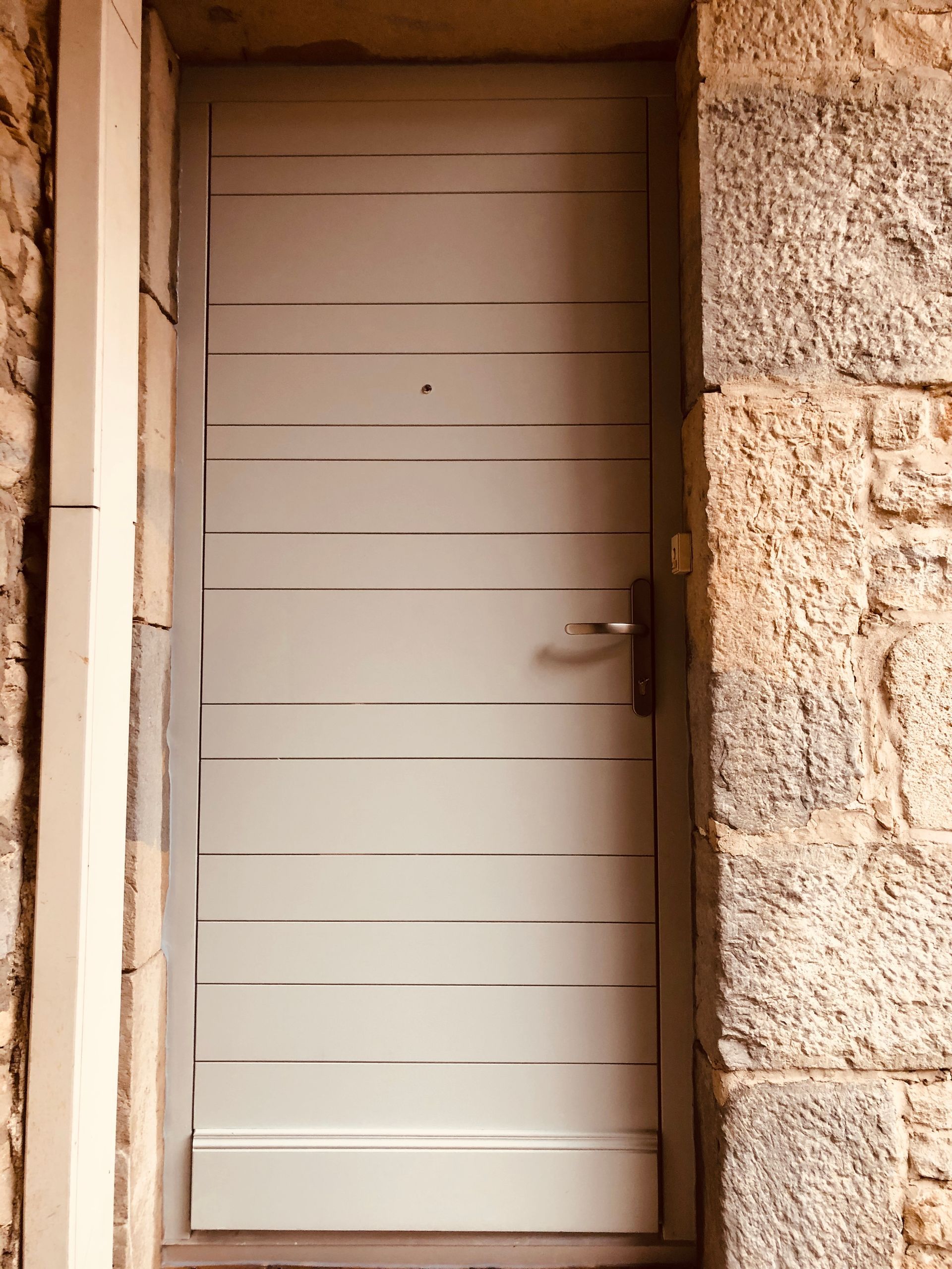 Porte blanche à rayures horizontales encastrée dans une ouverture dans un mur de pierre.