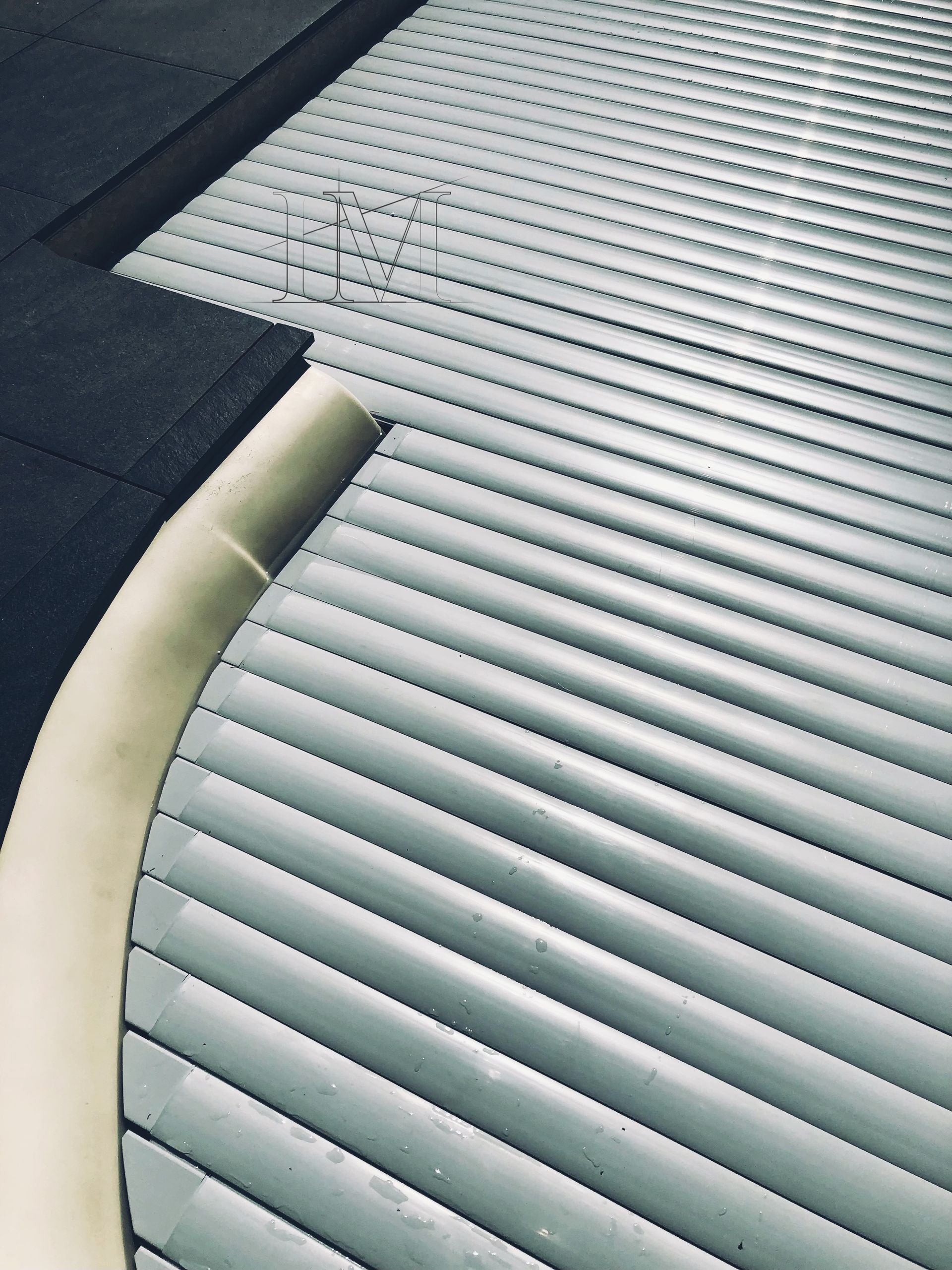 Couverture de piscine en lattes de bois beiges, partiellement enroulée, sur une eau bleue.
