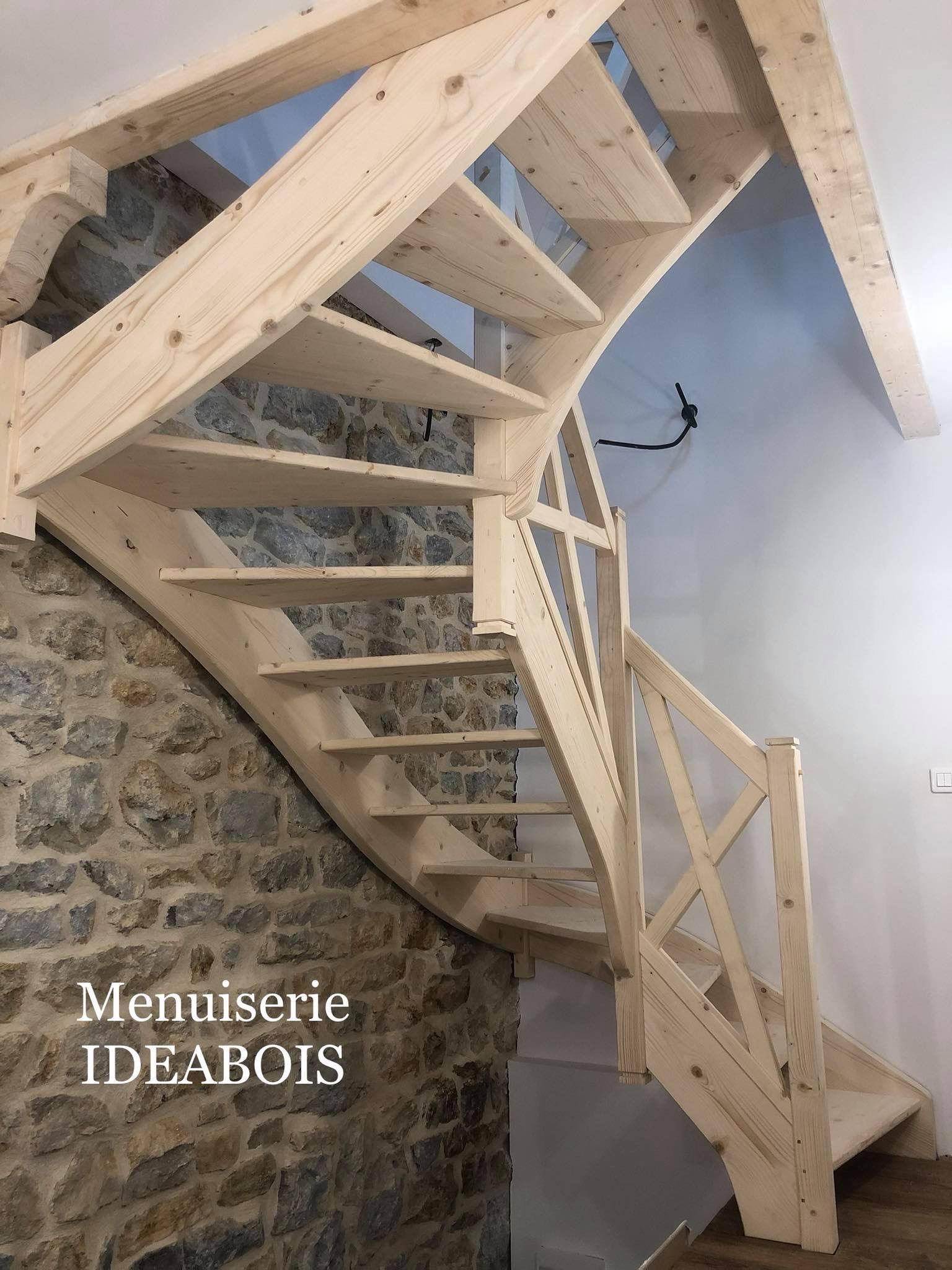 Escalier en bois aux lignes courbes, intégré dans une pièce aux murs de pierre et blancs.