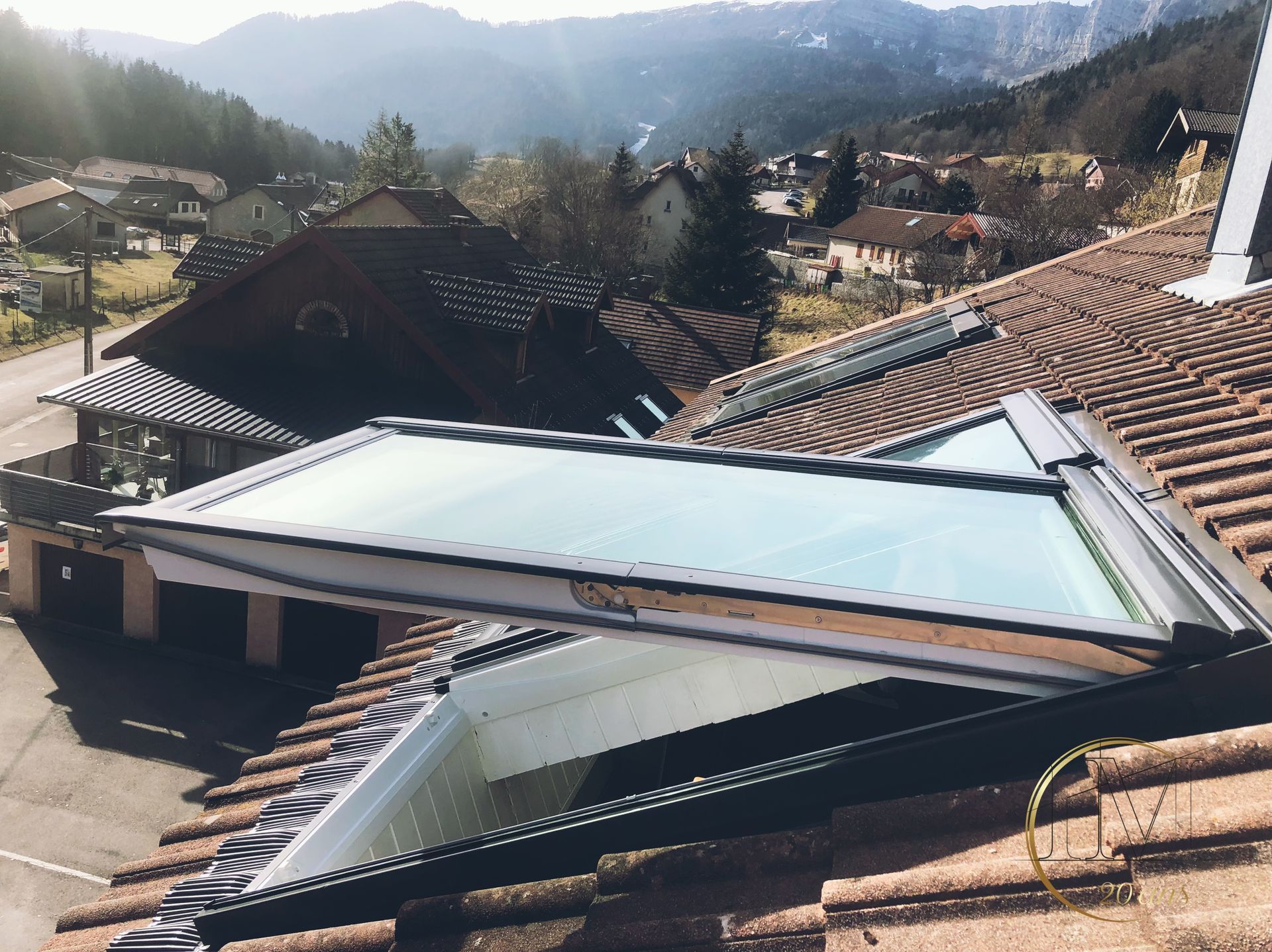 Puits de lumière ouvert sur un toit de tuiles avec vue sur la montagne, journée ensoleillée.