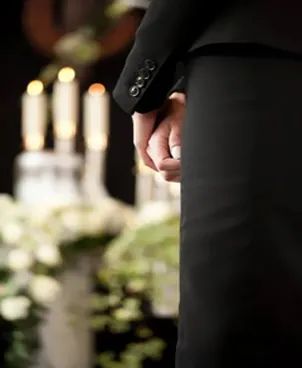 Un hombre con traje sostiene la mano de una mujer en un funeral.