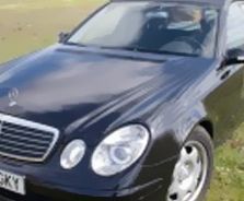 Un Mercedes Benz negro está estacionado en un campo de hierba.