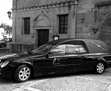 Una fotografía en blanco y negro de un coche fúnebre estacionado frente a un edificio.