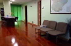 Una sala de espera con suelo de madera, sillas, una mesa y un cuadro en la pared.