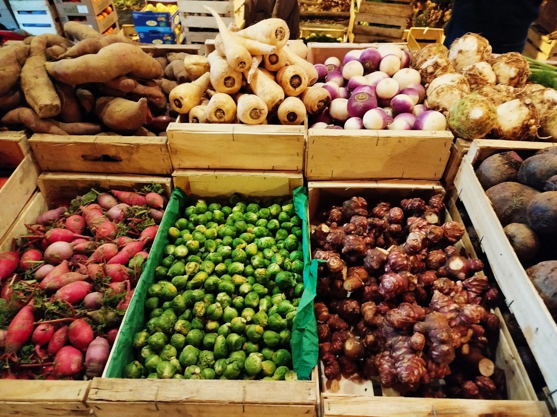Légumes sur un marché fermier : tomates, poivrons, concombres et aubergines. Les gens flânent sous des parasols blancs.