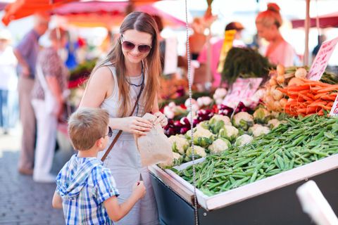 Une femme et son enfant achètent des produits frais sur un marché en plein air ; des légumes colorés sont exposés.