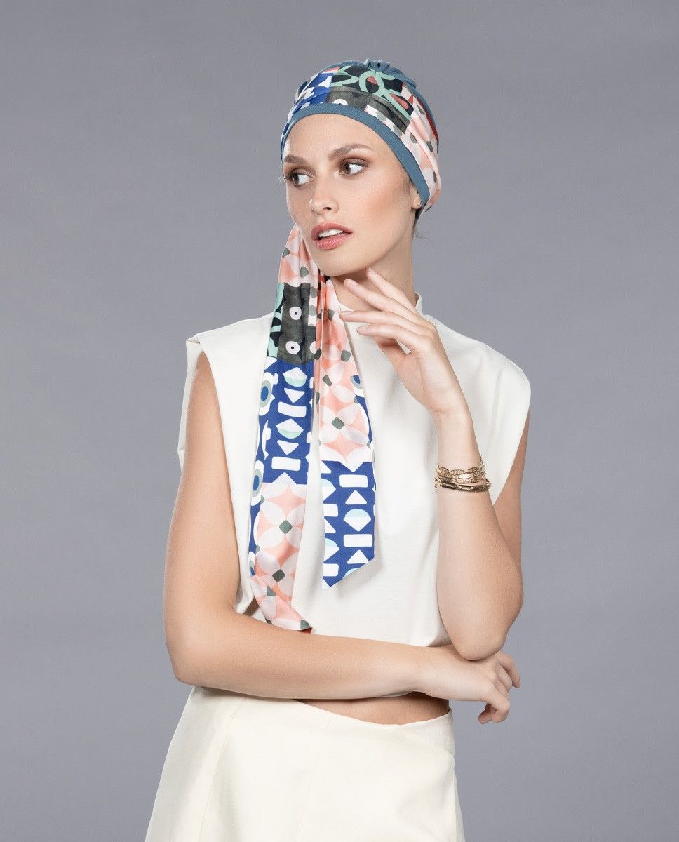 Frau mit gemustertem Kopftuch, weißem ärmellosem Oberteil und Rock, Blick zur Seite gerichtet.