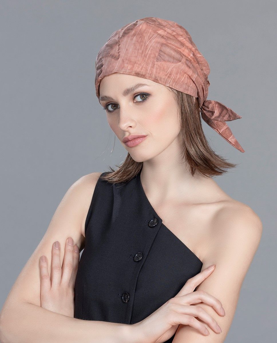 Frau mit rosa Kopftuch und schwarzem Oberteil, die Arme verschränkt, blickt nach vorne.