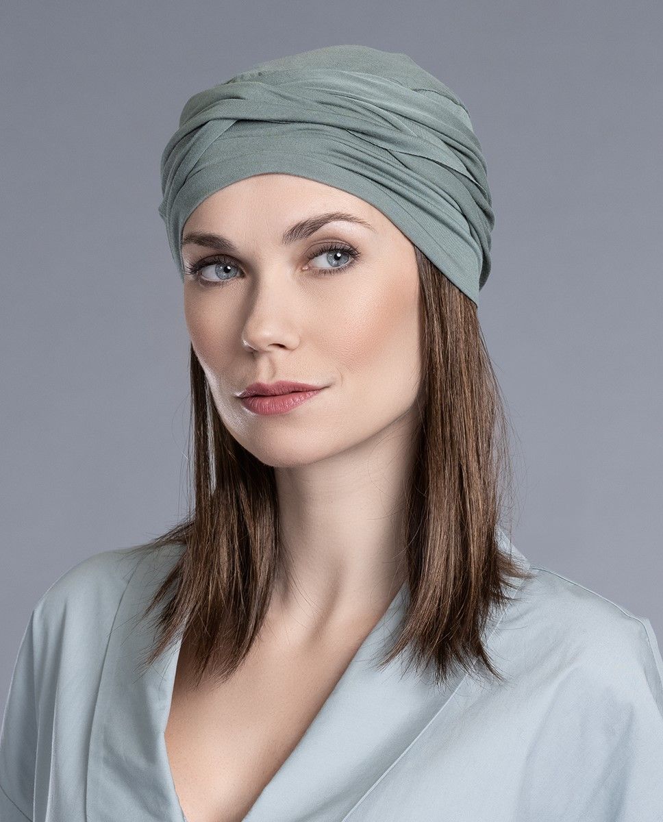 Frau mit blaugrünem Turban und schulterlangem braunem Haar, trägt ein passendes Oberteil und blickt nach oben.