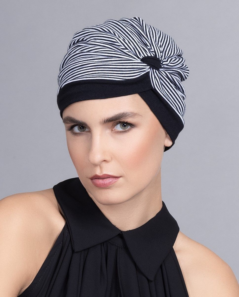 Frau mit schwarz-weiß gestreiftem Hut im Turban-Stil und schwarzem Oberteil.