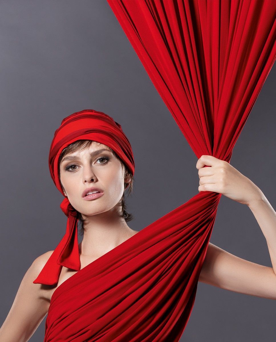 Frau mit rotem Kopftuch und drapiertem Stoff, die nach oben blickt und den Stoff in der Hand hält.