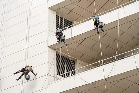 Tres limpiadores de ventanas con cuerdas suspendidas de un edificio, fregando la fachada.
