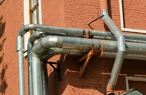 Tubos de metal galvanizado en el exterior de un edificio de ladrillo rojo, en ángulo y unidos con soportes.