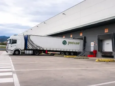 Interior del almacén con pilas de mercancía empaquetada sobre palés. Se ve una carretilla elevadora a la izquierda.
