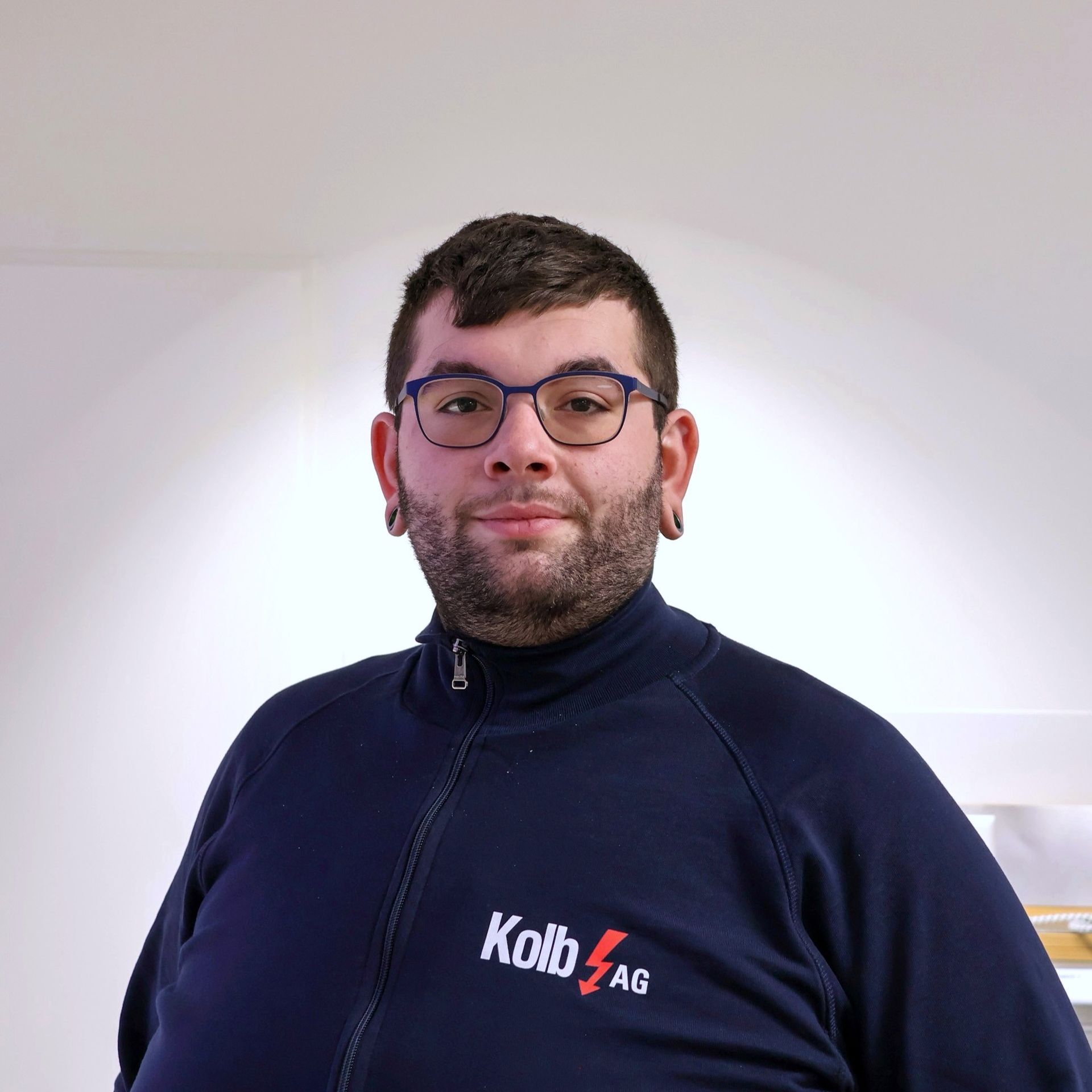 Mann mit Brille, blauer Reißverschlussjacke mit „Kolb AG“-Logo, blickt in die Kamera.